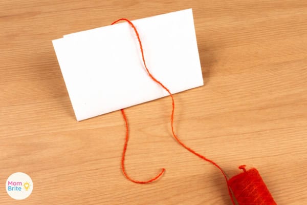 Red yarn laid across a small piece of cardboard to start making a tassel
