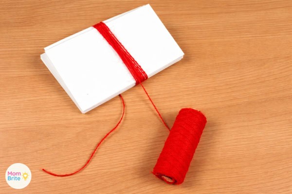 Red yarn wrapped around cardboard piece for DIY bookmark tassel