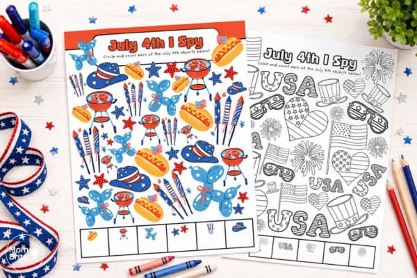 Two July 4th I Spy printable activity sheets for kids displayed side by side. The colorful version features red, white, and blue illustrations of hot dogs, fireworks, grills, balloons, and stars, while the black and white version shows USA letters, patriotic hats, flag hearts, and sunglasses to color and count. Surrounded by markers, crayons, patriotic ribbon, and star confetti.